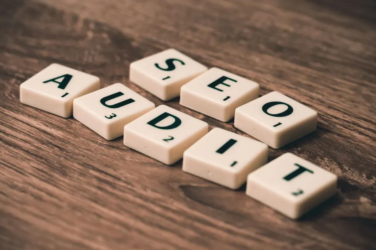 Peças de letras sobre mesa de madeira formando as palavras SEO e AUDIT