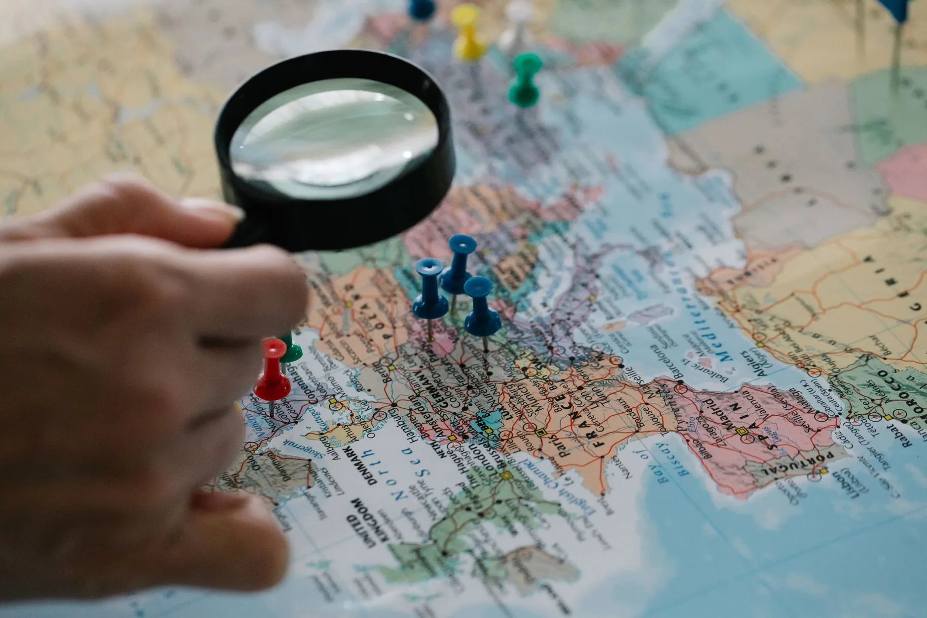 Pessoa usando uma lupa sobre um mapa com alfinetes marcando locais