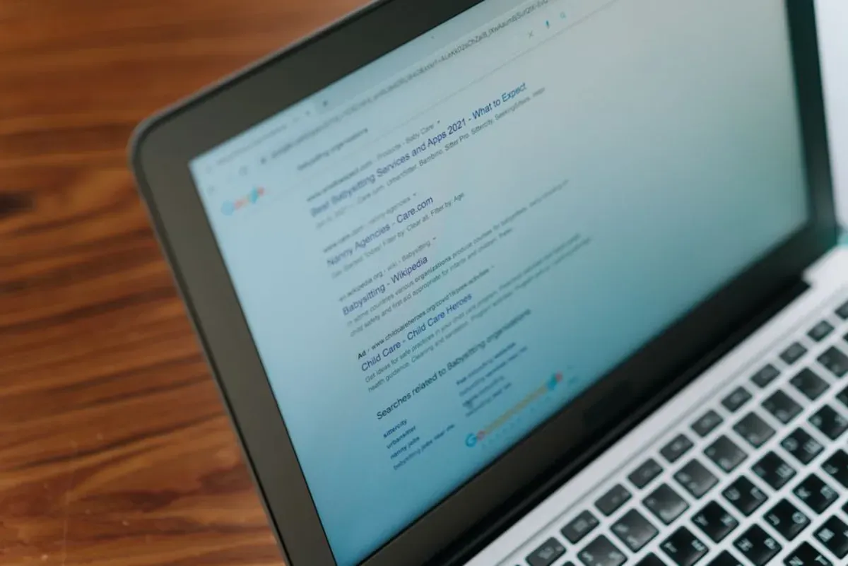 Imagem de um laptop em uma mesa de madeira exibindo resultados de pesquisa na internet, ideal para abordar temas de pesquisa online ou uso de tecnologia na rotina diária.