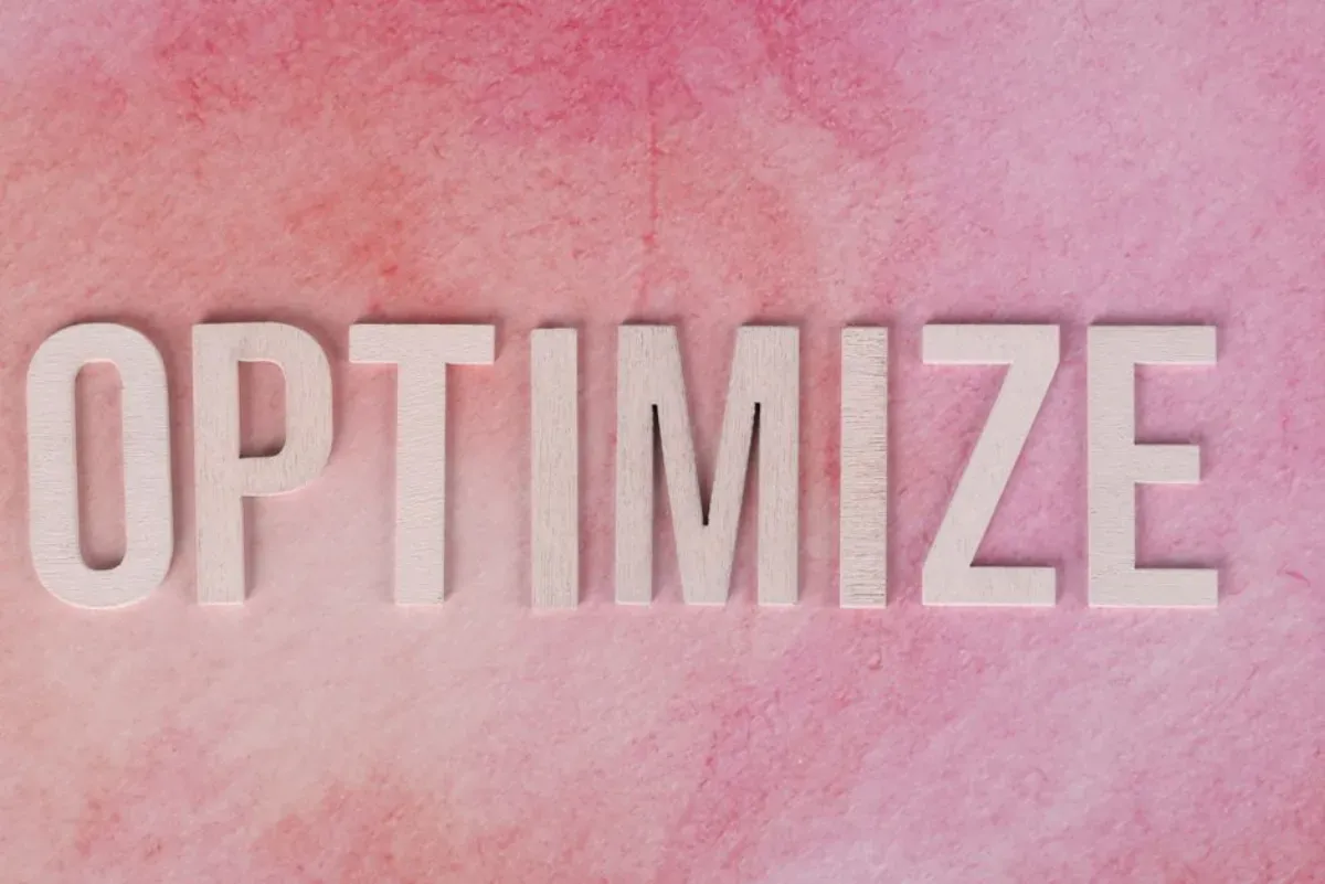 Letra em relevo formando a palavra ‘OPTMIZE’ sobre fundo de tom rosa, simbolizando inovação e otimização de processos.