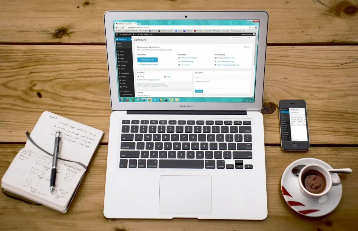 Notebook com um editor de site aberto, ao lado de caderno, celular e café