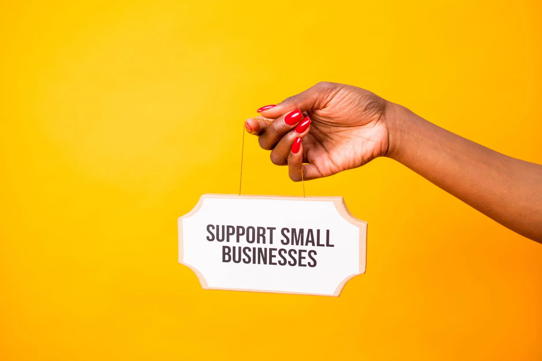 Mão segurando uma placa escrita Support Small Businesses sobre fundo amarelo