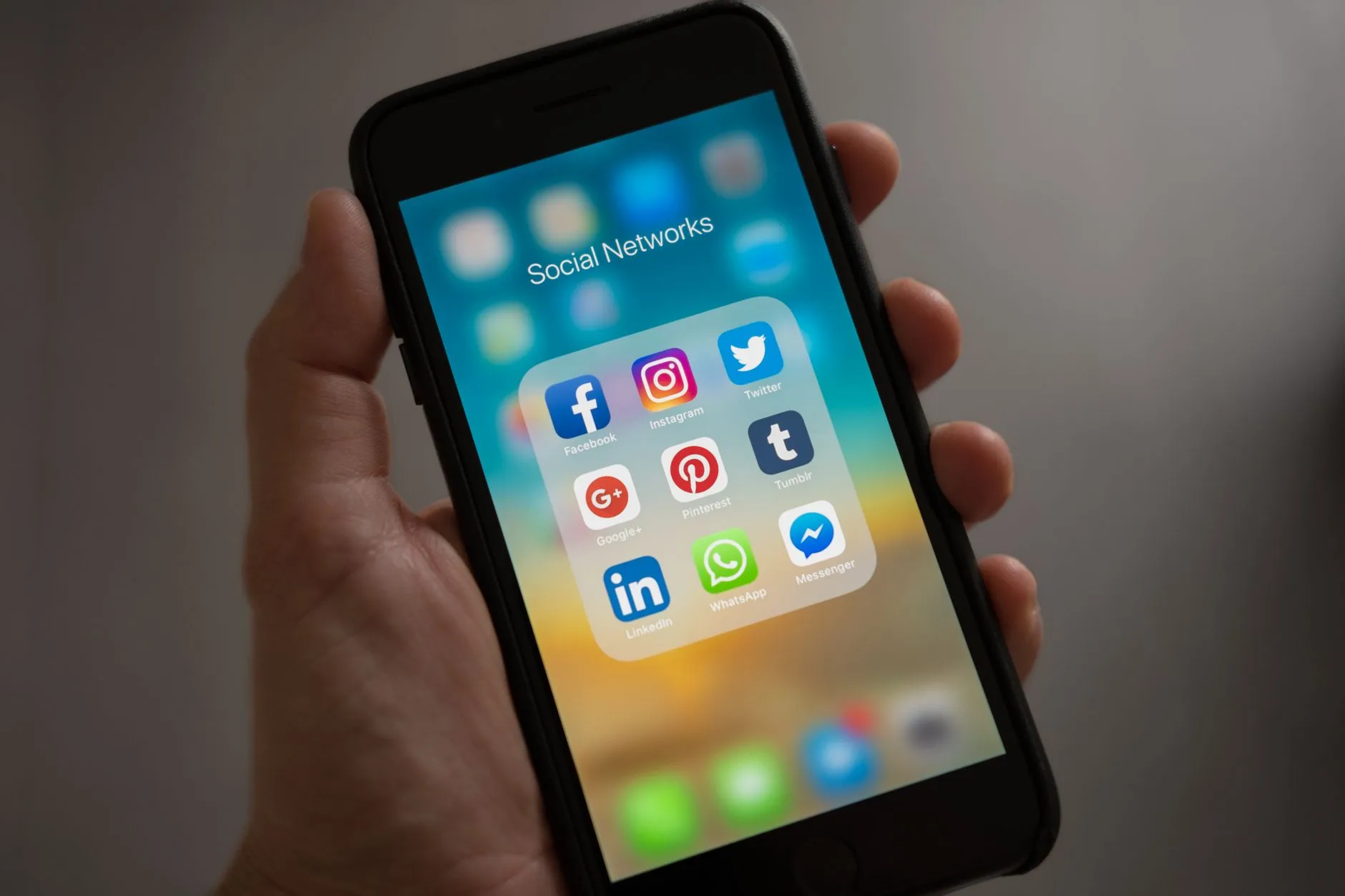Mão segurando um celular com a pasta de aplicativos de redes sociais aberta