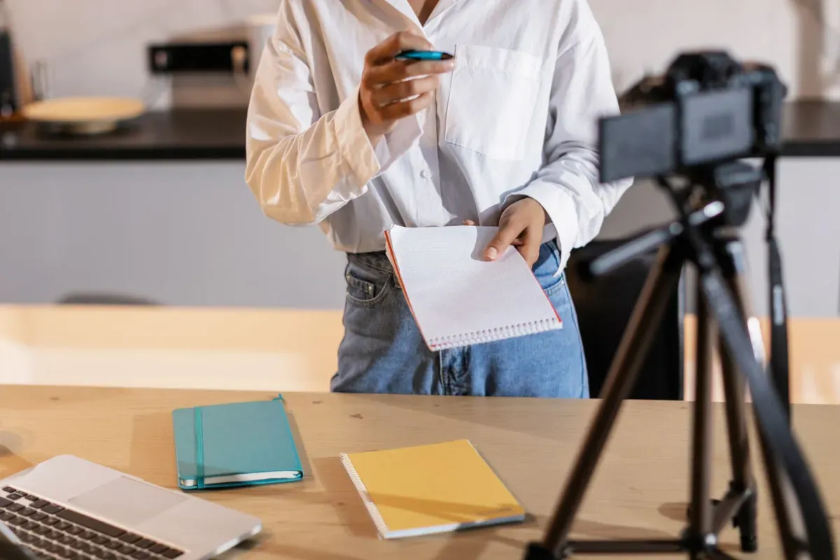 Criadora de conteúdo gravando um vídeo com câmera, anotações e notebook