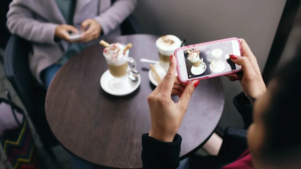 Duas mulheres fotografando cafés com o celular em uma cafeteria