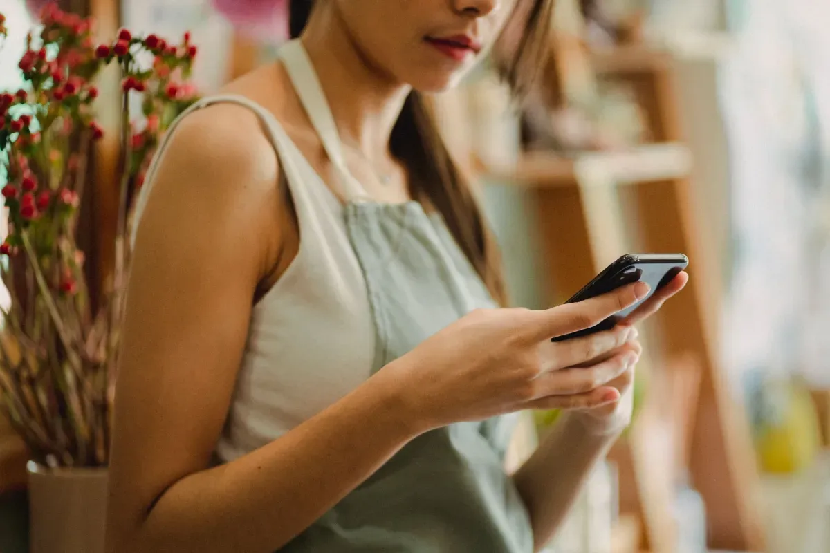 Comerciante de avental usando o celular dentro da própria loja