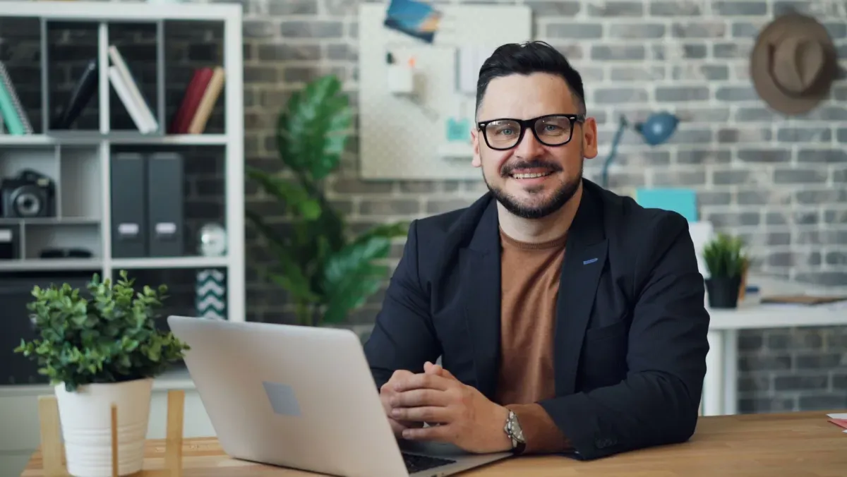 Empreendedor sorridente de óculos sentado diante do notebook em um escritório