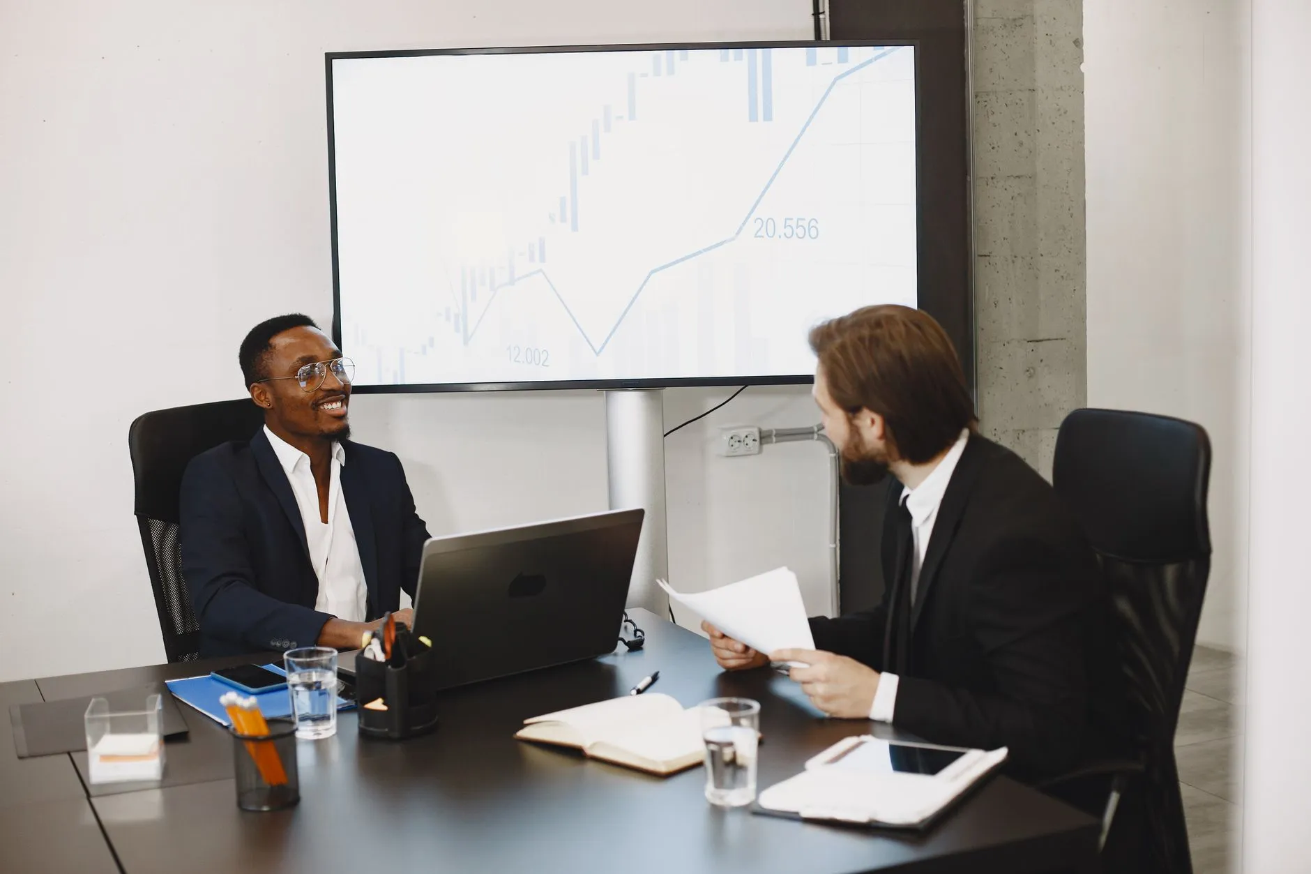 Dois profissionais conversando em uma sala de reunião com notebook